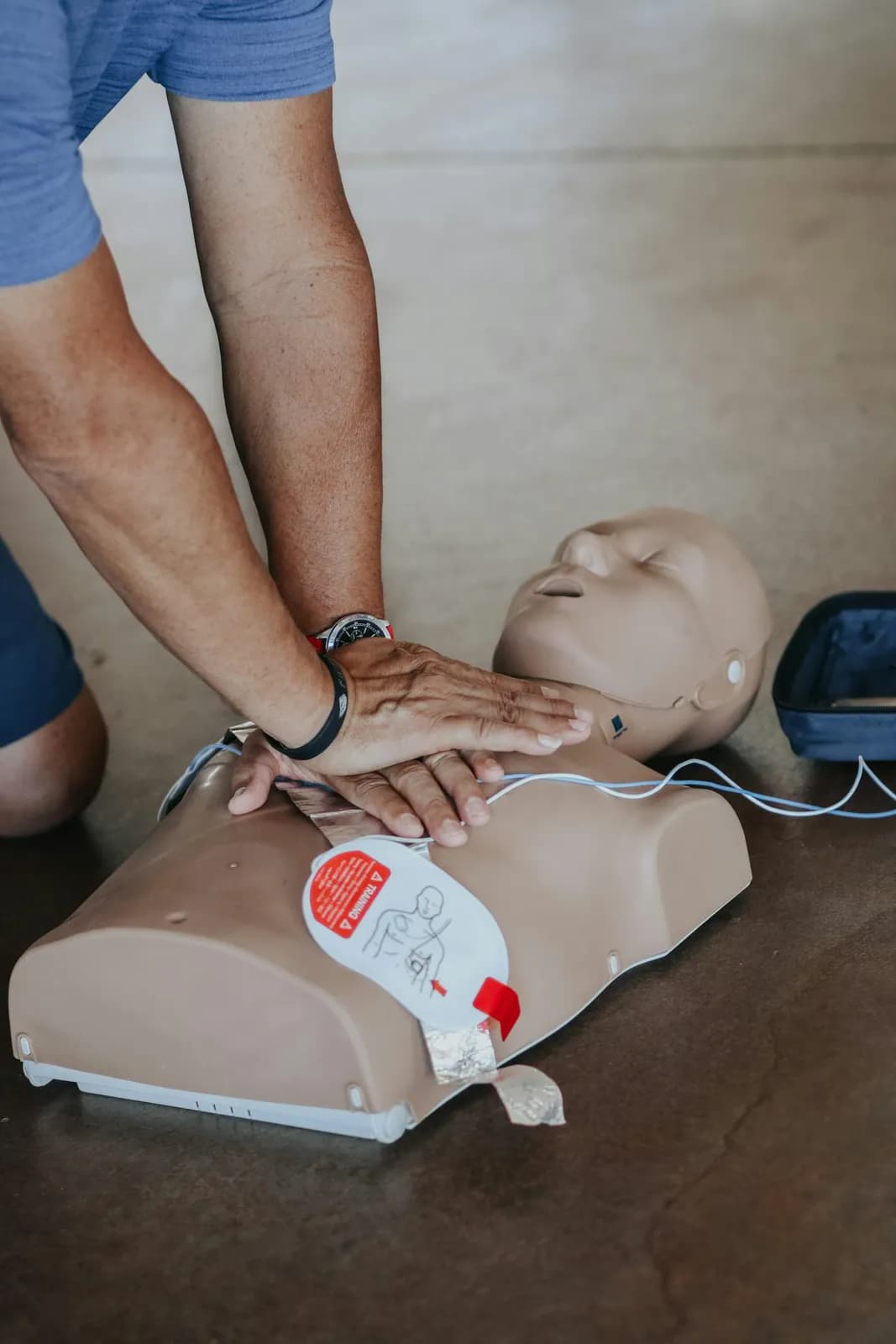 Mains effectuant un massage cardiaque sur mannequin de formation avec DAE